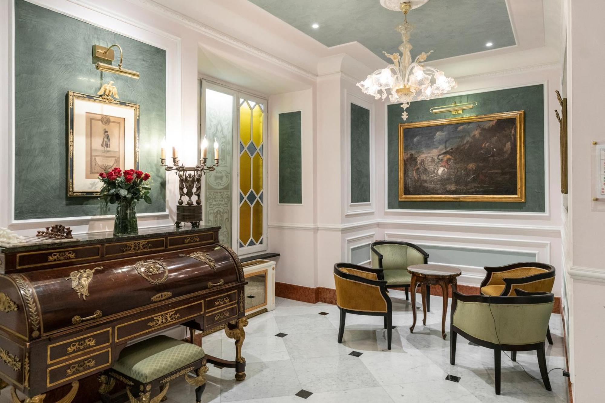Hotel Bristol Palace Генуя Экстерьер фото The photo shows a beautifully decorated interior space that appears to be a small living or reception area. It features elegant furniture, including a wooden writing desk or chest with intricate designs and several chairs with a mix of colors. 

The 