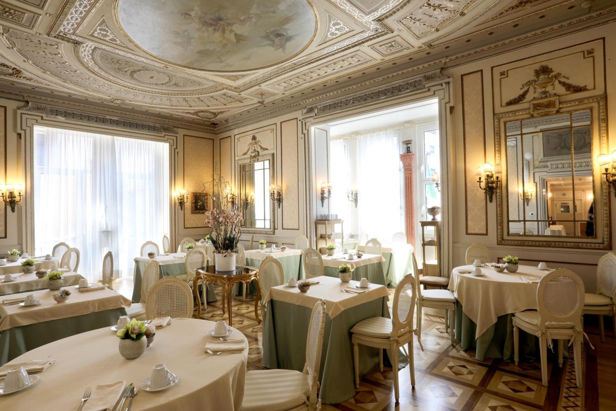 Hotel Bristol Palace Генуя Экстерьер фото The photo shows an elegant dining room featuring a refined interior design. The space has intricately detailed walls and a beautifully adorned ceiling, likely showcasing classical architectural elements. 

There are several round tables set with ligh