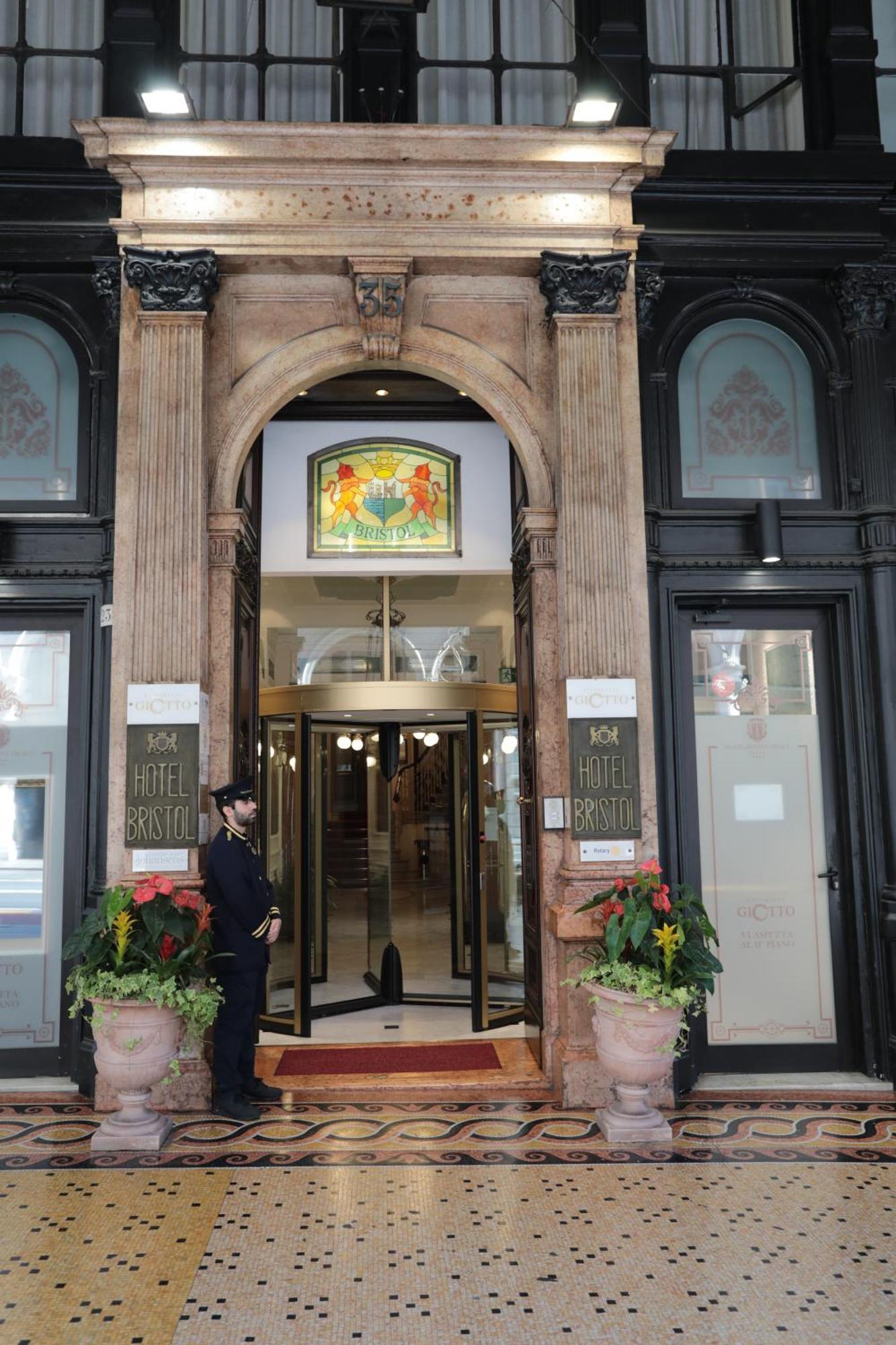 Hotel Bristol Palace Генуя Экстерьер фото The photo shows the entrance of a hotel, specifically the "Hotel Bristol." The entrance features an ornate archway with decorative elements. Above the main door, there is a stained glass window with colorful designs. To the sides of the entrance, the