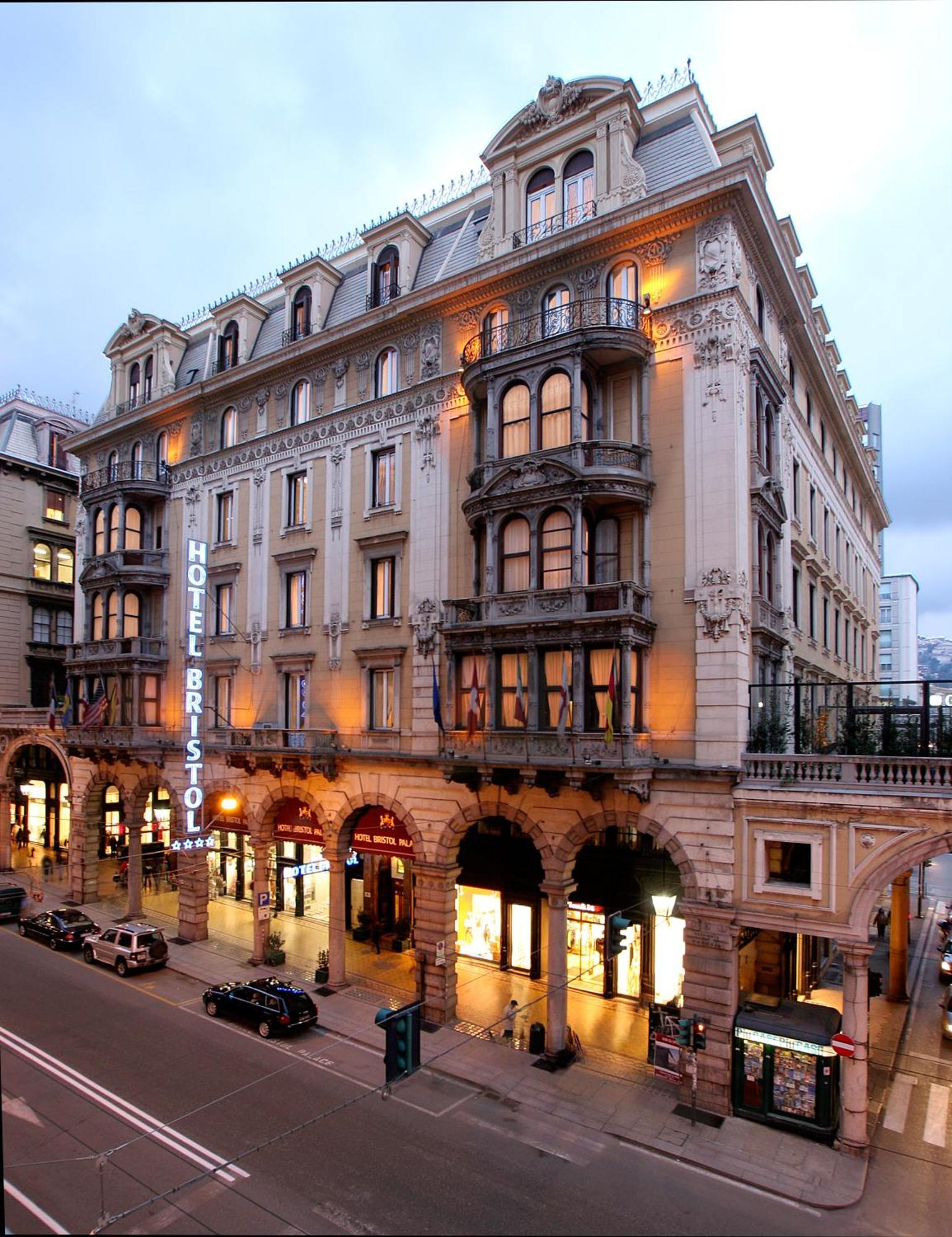 Hotel Bristol Palace Генуя Экстерьер фото The photo shows a grand hotel building, likely the Hotel Bristol. It features an elegant architectural design with ornate details, including balconies and decorative moldings. The façade is illuminated, giving it a warm glow in the evening light. The