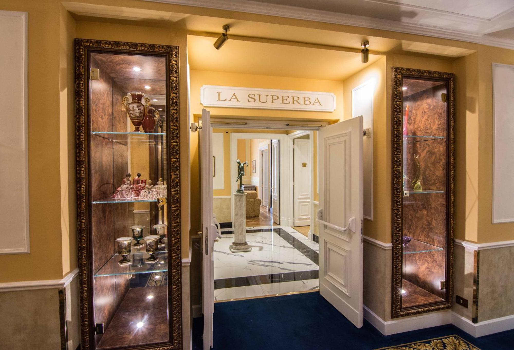 Hotel Bristol Palace Генуя Экстерьер фото The photo shows the entrance to a venue or restaurant named "La Superbia." The entrance features double doors that are open, revealing an elegant interior. Flanking the entrance are glass display cases with ornate decorations, which likely showcase f