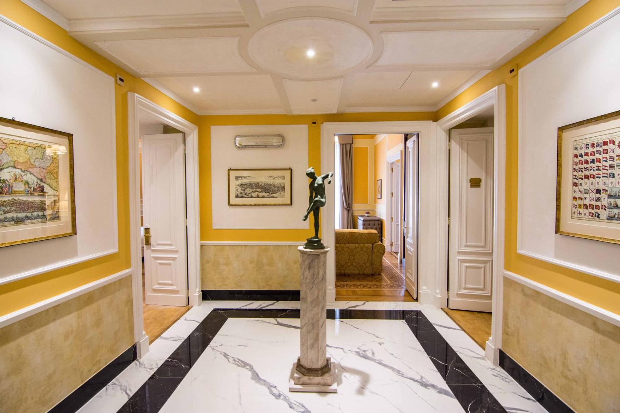 Hotel Bristol Palace Генуя Экстерьер фото The photo shows an elegant hallway with a bright yellow wall and marble flooring. The ceiling is detailed, featuring a circular design. In the center, there is a statue on a small pedestal, adding a decorative touch to the space. The walls are adorne